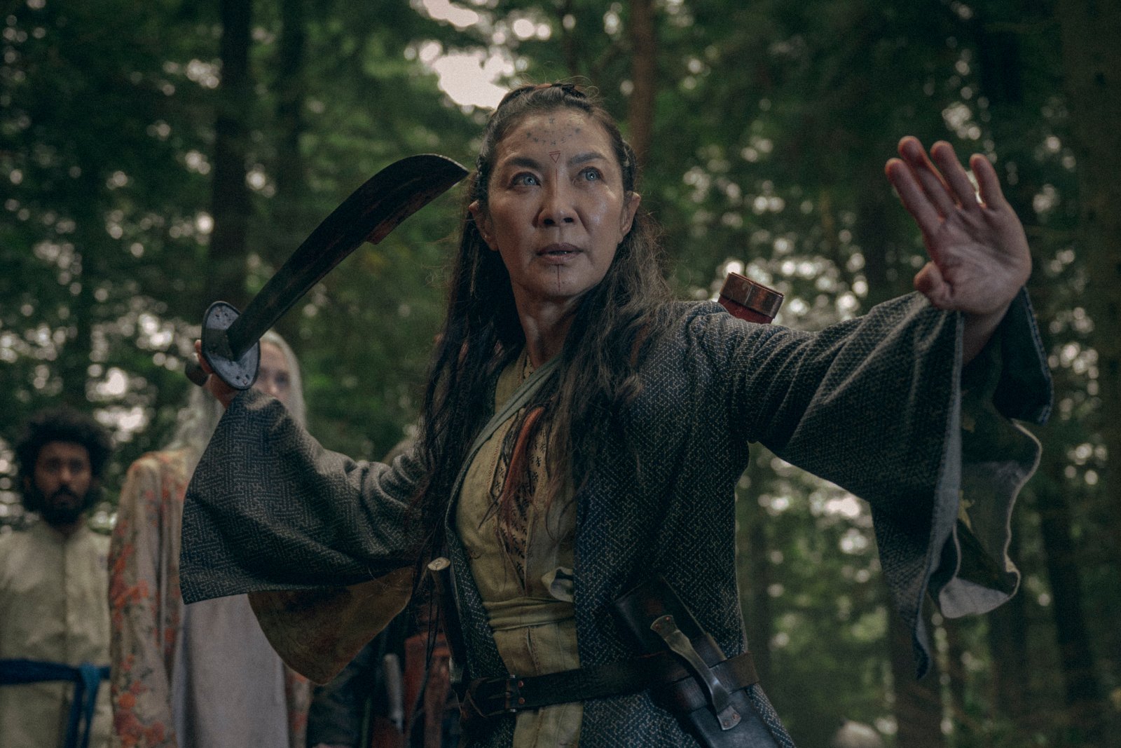 Michelle Yeoh in 'The Witcher: Blood Origin' for our article about its release time on Netflix. She's holding a sword and readying herself to fight.