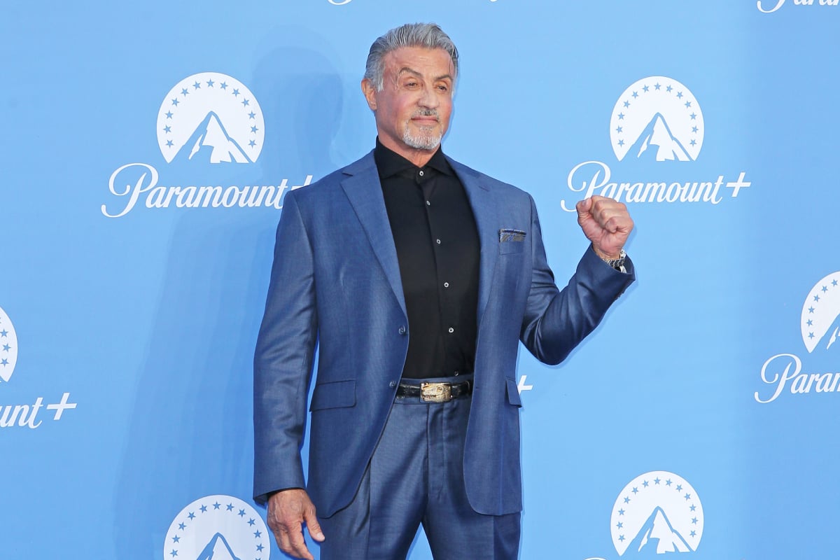 Tulsa King star Sylvester Stallone wears a blue suit with a black button-down shirt.