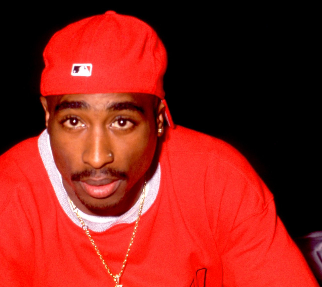 Tupac Shakur dazes into the camera wearing red and a gold chain