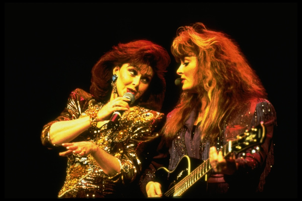 Mother and daughter duo Naomi and Wynonna Judd singing in concert c. 1990. Wynonna called her relationship with Naomi a “love affair” that will never end.