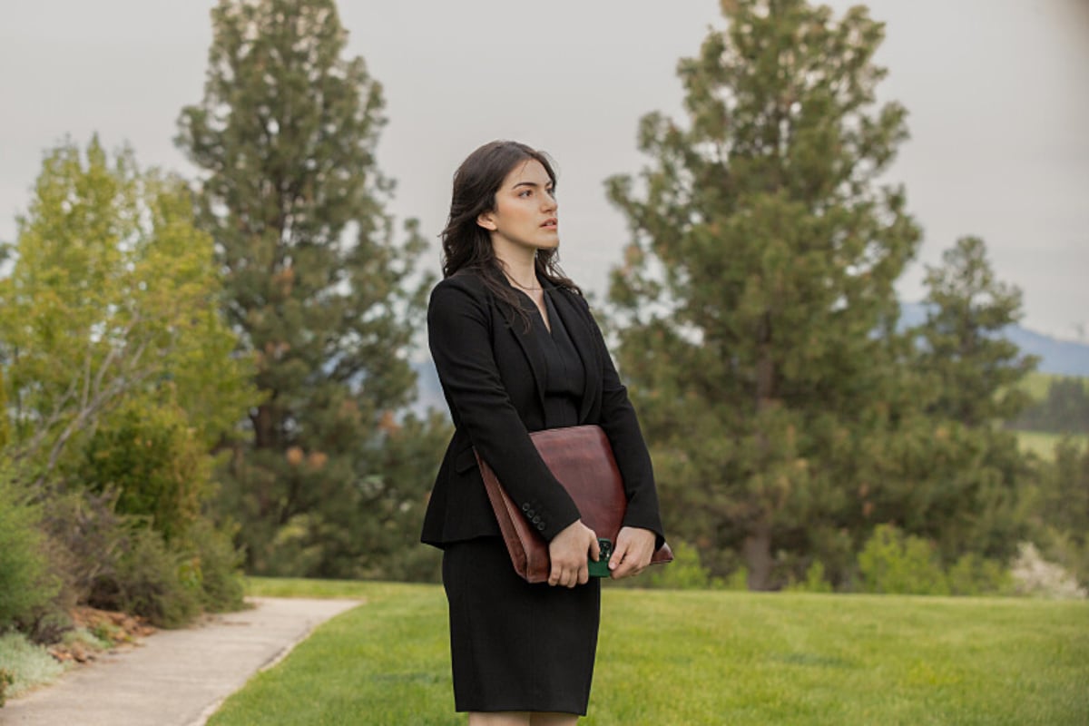 In Yellowstone, Clara Brewer wears a black skirt and blazer and holds a briefcase. 