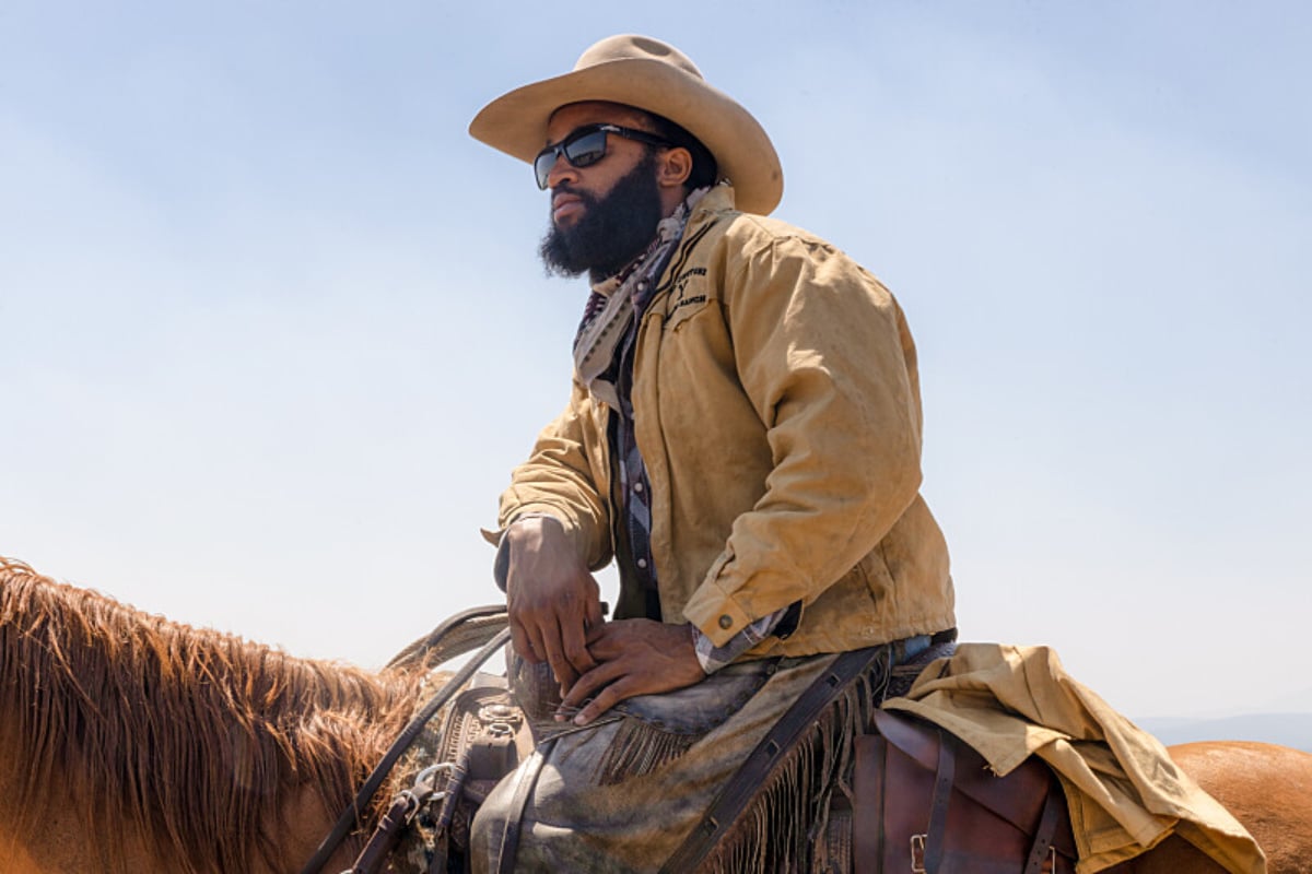 The cast of Yellowstone worked long hours to film the spring gathering. Denim Richards sits on a horse wearing a cowboy hat and sunglasses.