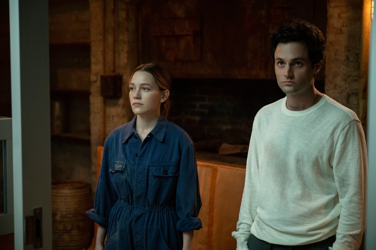 In You Season 3, Victoria Pedretti and Penn Badgley stand in the basement of the bakery as Joe and Love.