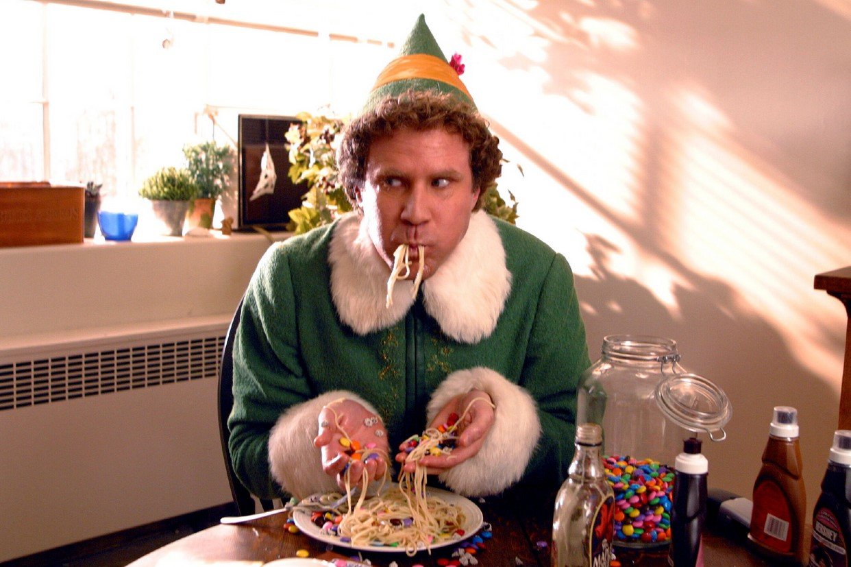 Will Ferrell, in character as Buddy in 'Elf,' one of the Christmas movies fans watch every year, wears his green elf costume while eating spaghetti.