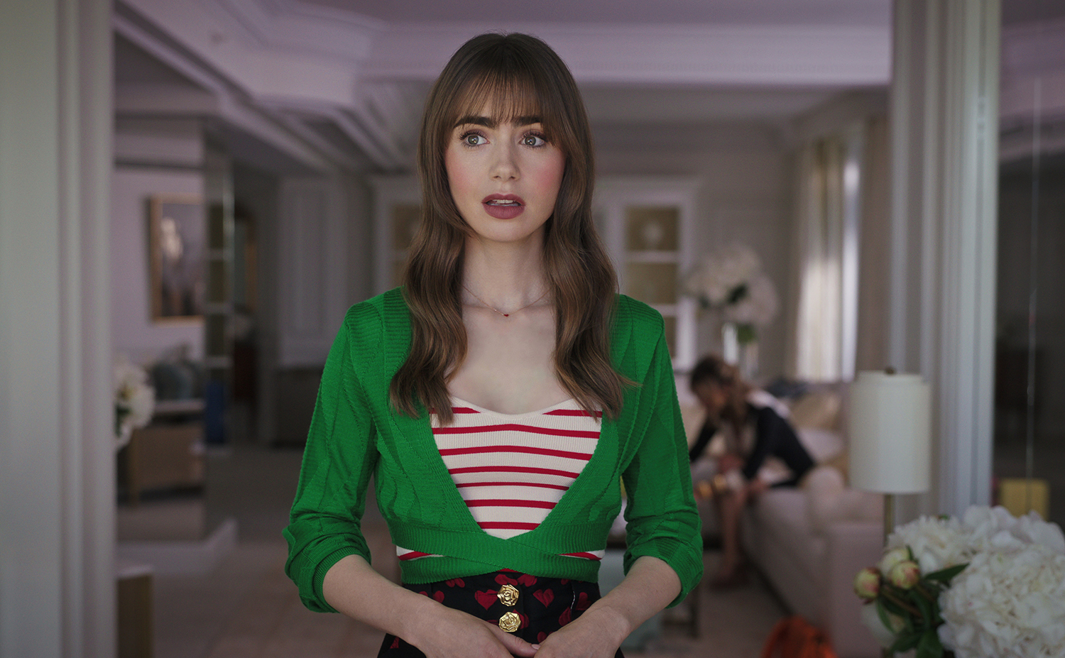 Emily in Paris Season 3: Lily Collins as Emily Cooper wearing a red and white striped tank top with a bright green shirt and looking shocked.