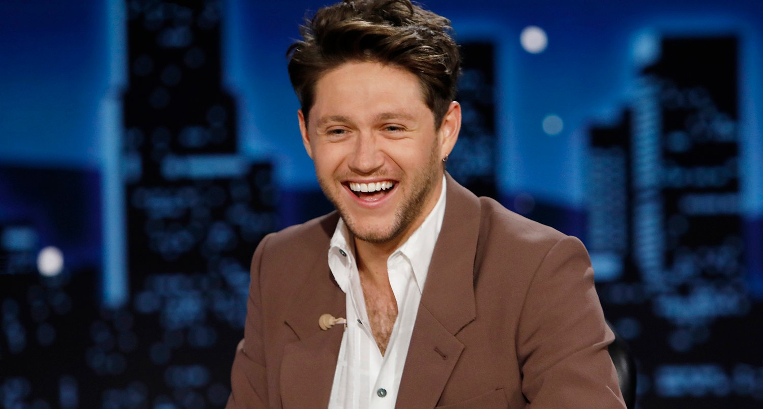 The Voice coach Niall Horan smiles in a brown suit on Jimmy Kimmel Live in August 2022.