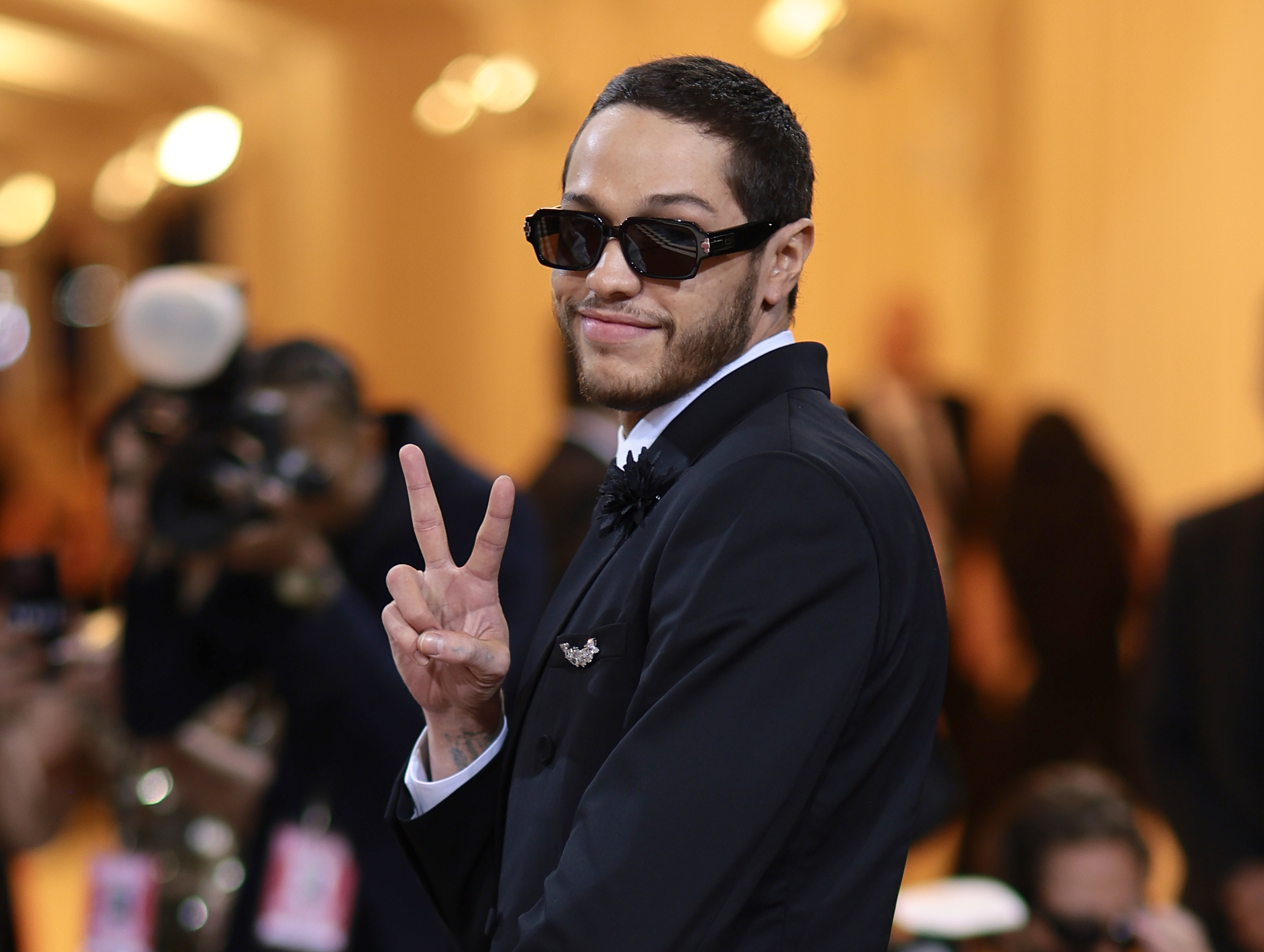 Pete Davidson attends The 2022 Met Gala while wearing sunglasses and making the peace sign.