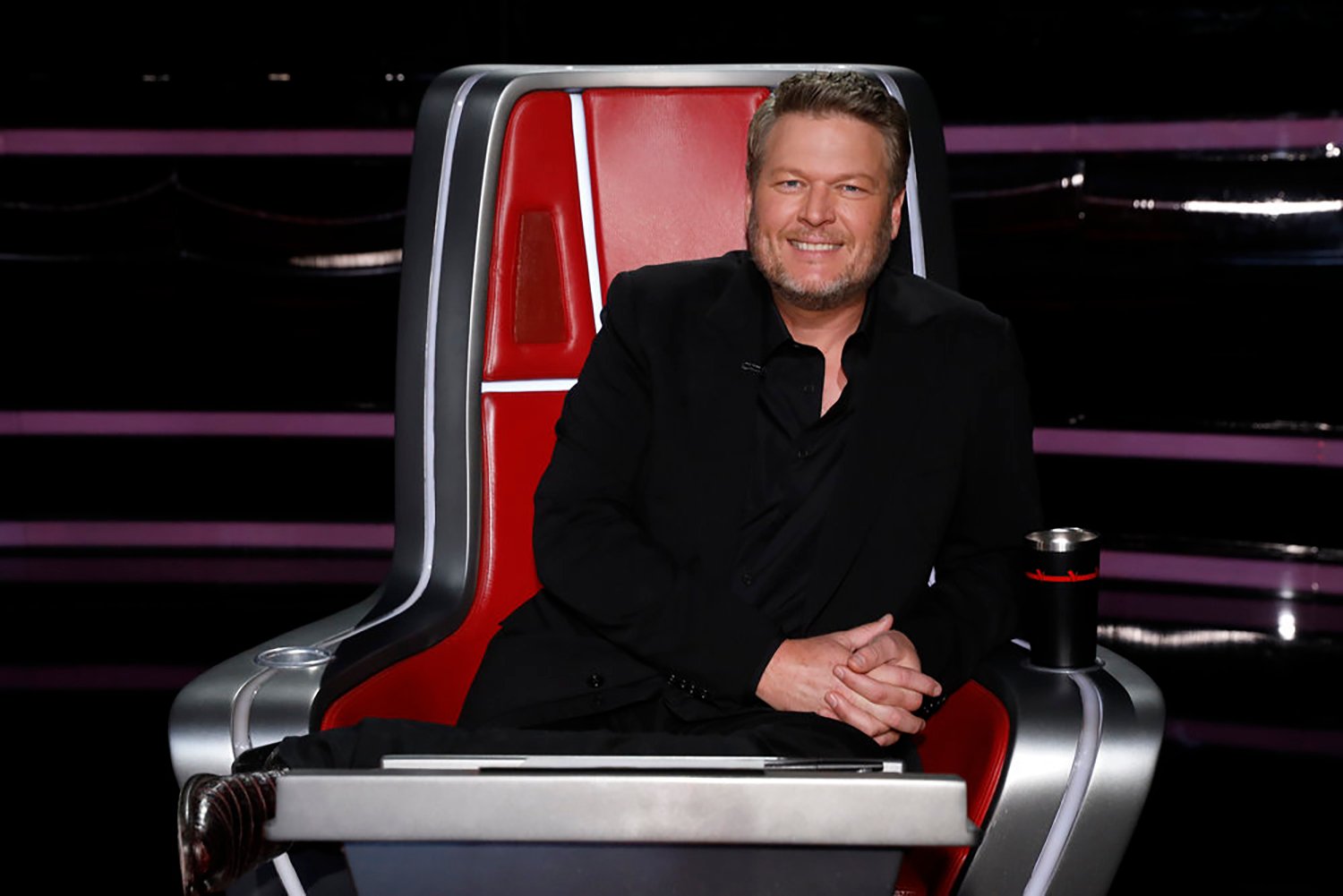 Blake Shelton smiles in his seat on The Voice Season 22 one night before he wins..