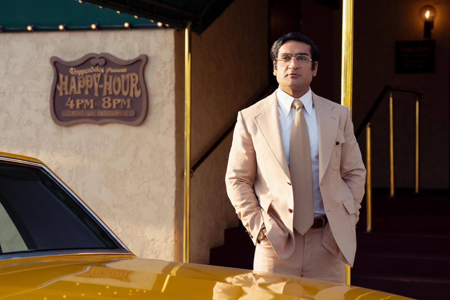 'Welcome to Chippendales' Steve Banerjee played by Kumail Nanjiani, standing in a beige suit beside a taxi in a prodution still.