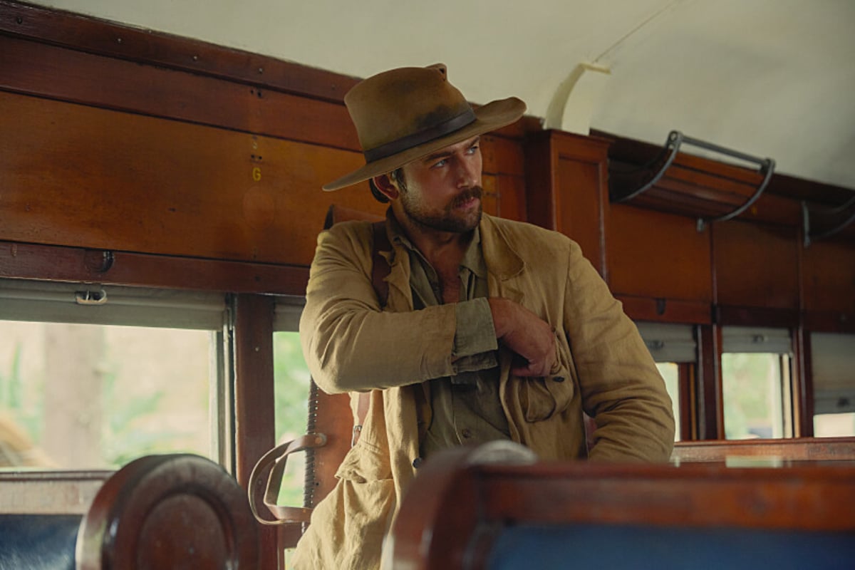 In 1923, Spencer Dutton stands in a train in Africa wearing a beige jacket and hat.