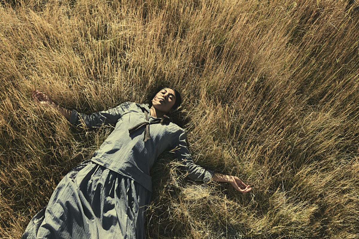 Aminah Nieves as her 1923 character Teonna lays in the grass wearing her boarding school uniform.