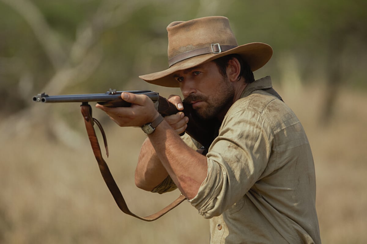 1923 includes several easter eggs and parallels to Yellowstone. Spencer Dutton points a rifle. He wears a beige hat and shirt.