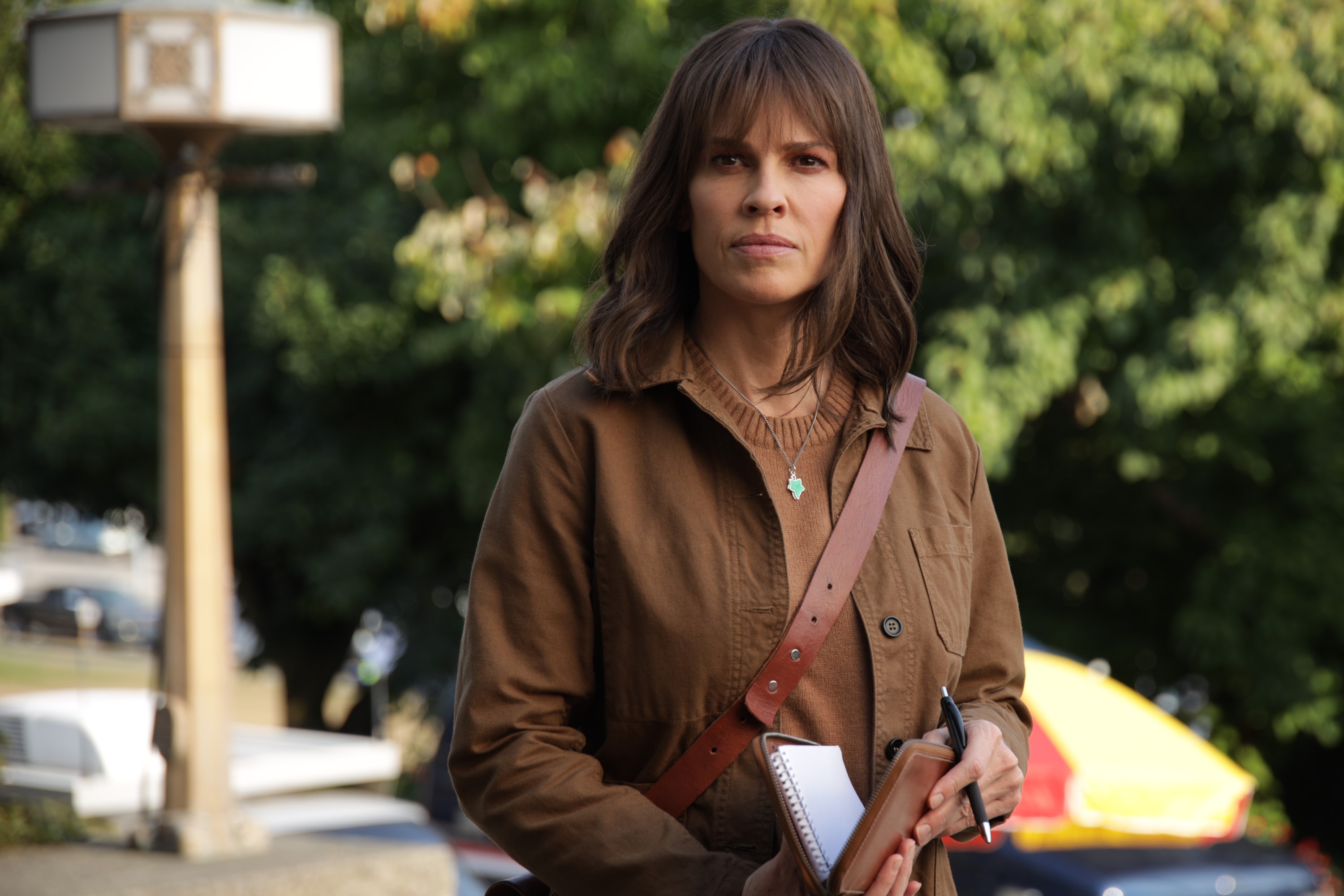 Hilary Swank, in character as Eileen Fitzgerald in 'Alaska Daily' on ABC, wears a brown coat over a brown sweater and holds a notepad.
