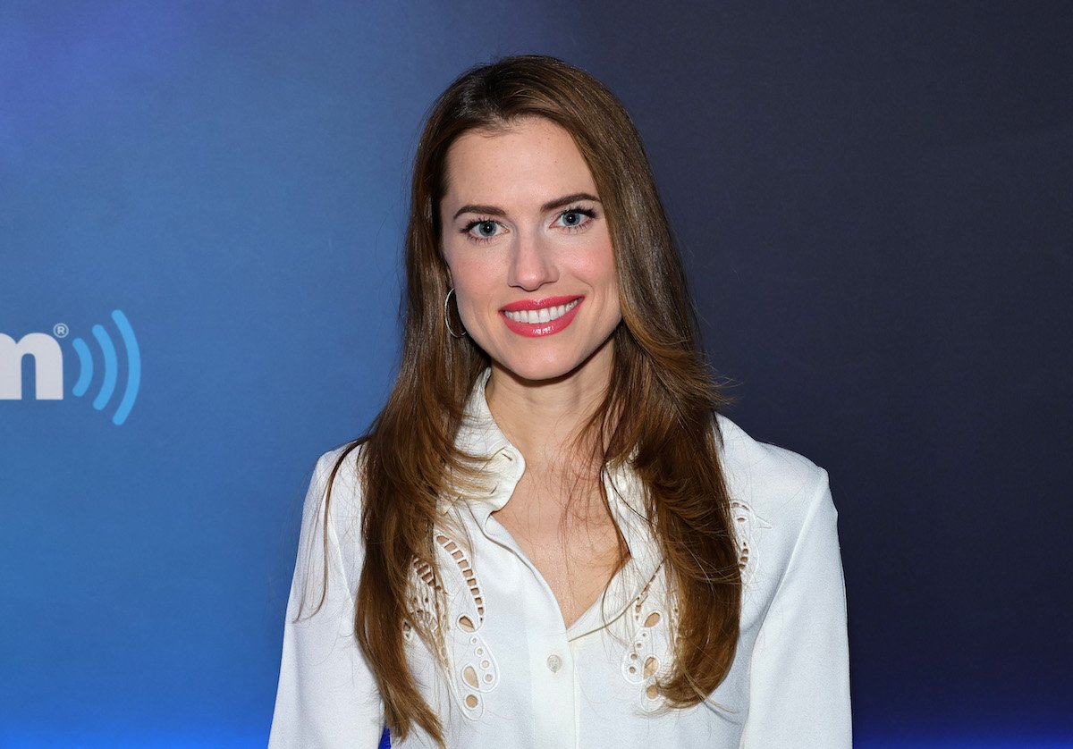 Allison Williams poses for the camera in front of a blue backdrop.