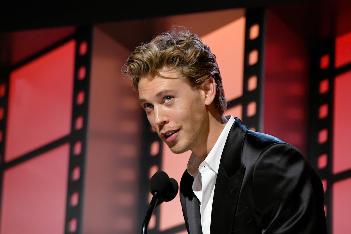 Austin Butler speaks into a microphone with lit up film strips in the background.