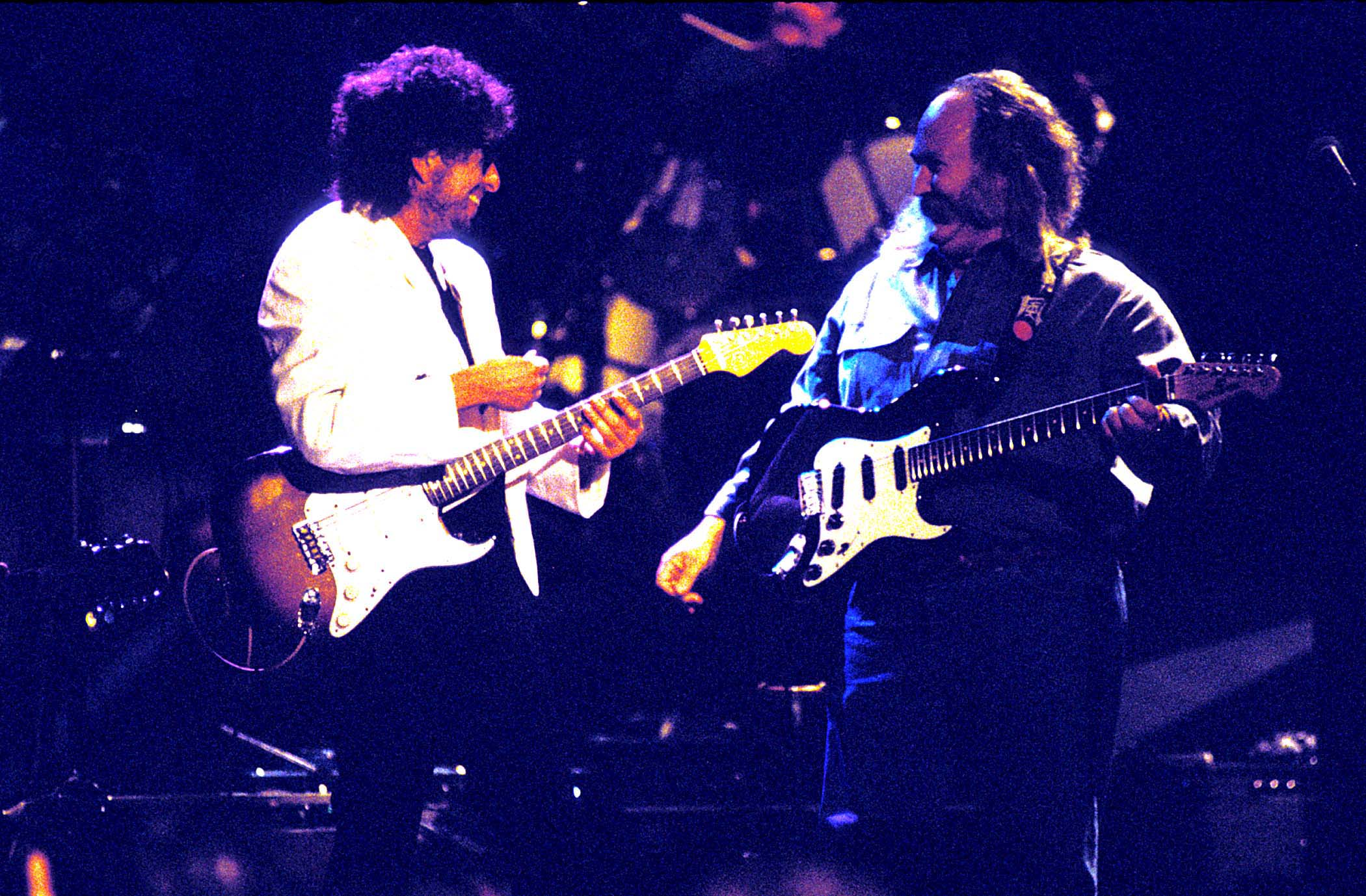 Bob Dylan and David Crosby hold guitars onstage together.