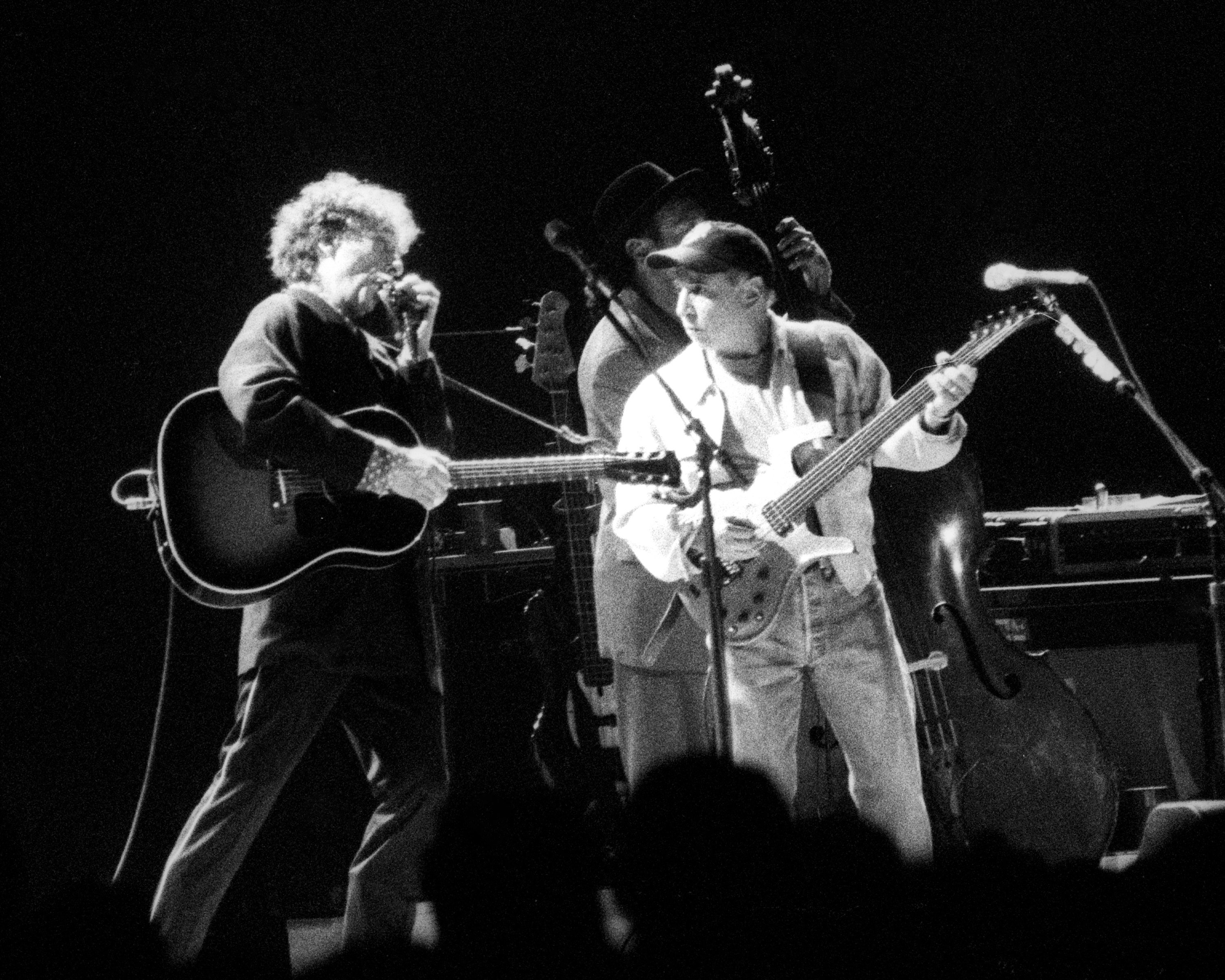 A black and white picture of Bob Dylan and Paul Simon playing guitars on stage together.