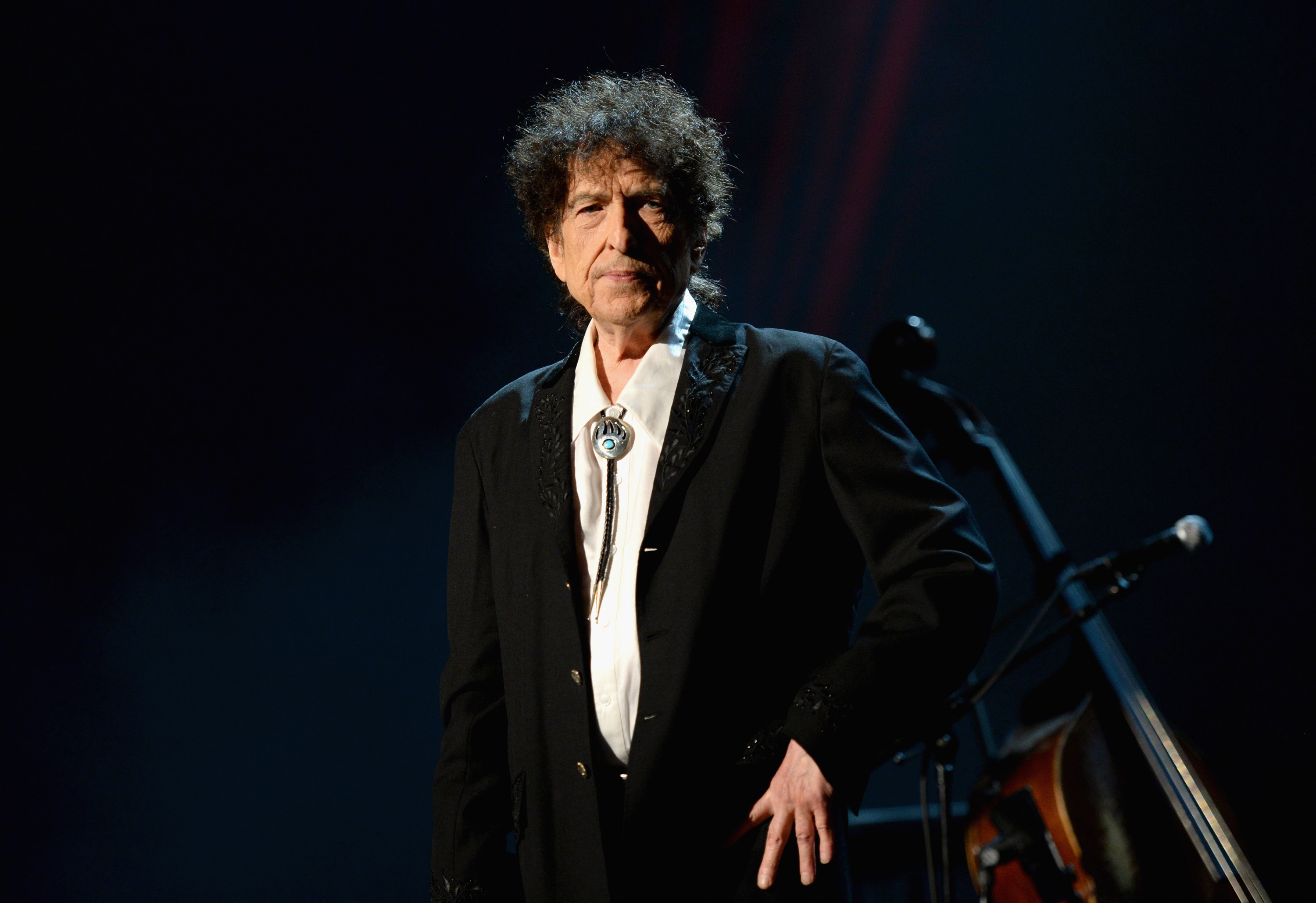 Bob Dylan wears a bolo tie and stands with his hand on his hip.