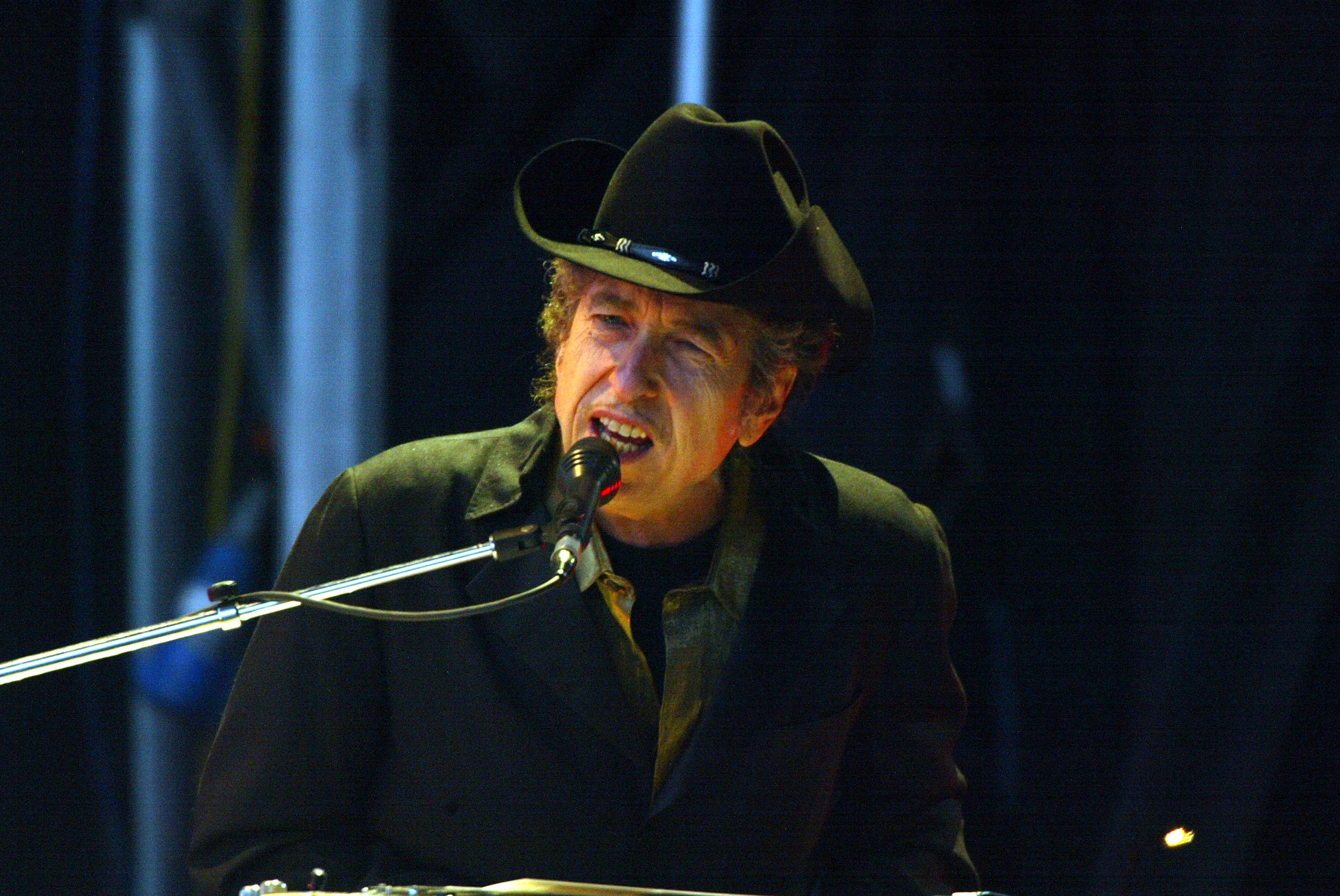 Bob Dylan wears a cowboy hat and sings into a microphone.