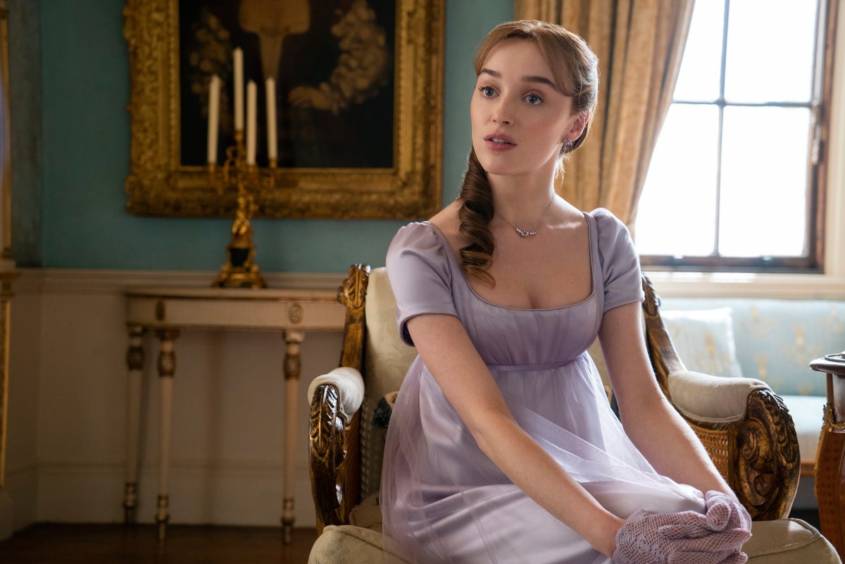 Wife of the Duke, Daphne Bridgerton wears a purple dress and sits on a chair.