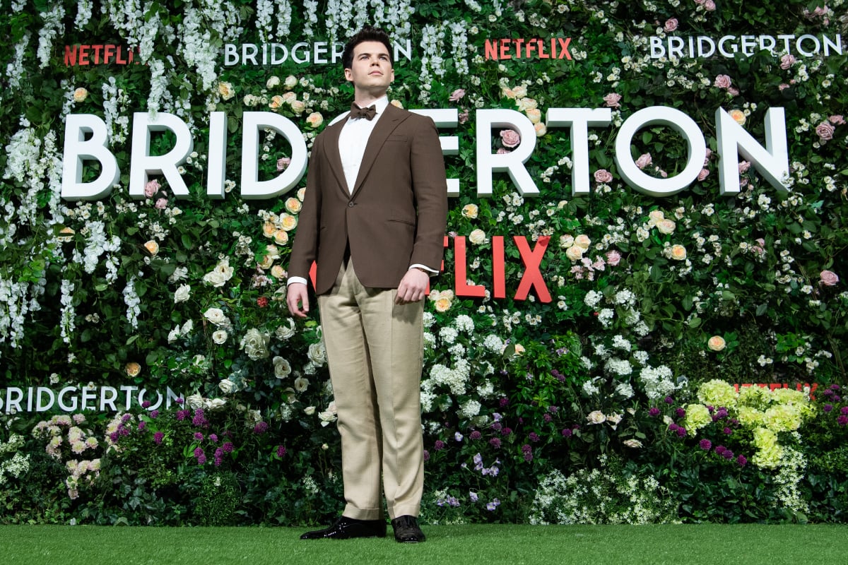Luke Newton attends the Bridgerton Season 2 world premiere wearing a brown suit jacket and bowtie.
