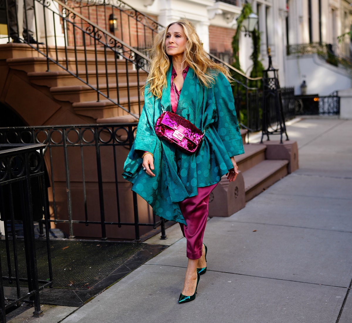 Sarah Jessica Parker as Carrie Bradshaw walks down a New York City street wearing magenta pants and an emerald green top during the filming of 'And Just Like That...' season 2