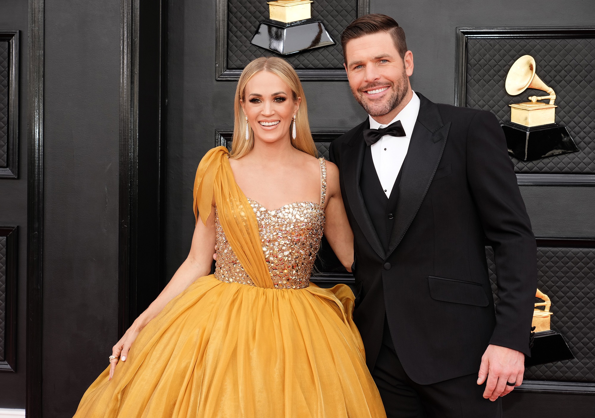 Carrie Underwood in an orange and glittery dress standing with Mike Fisher in a black tux