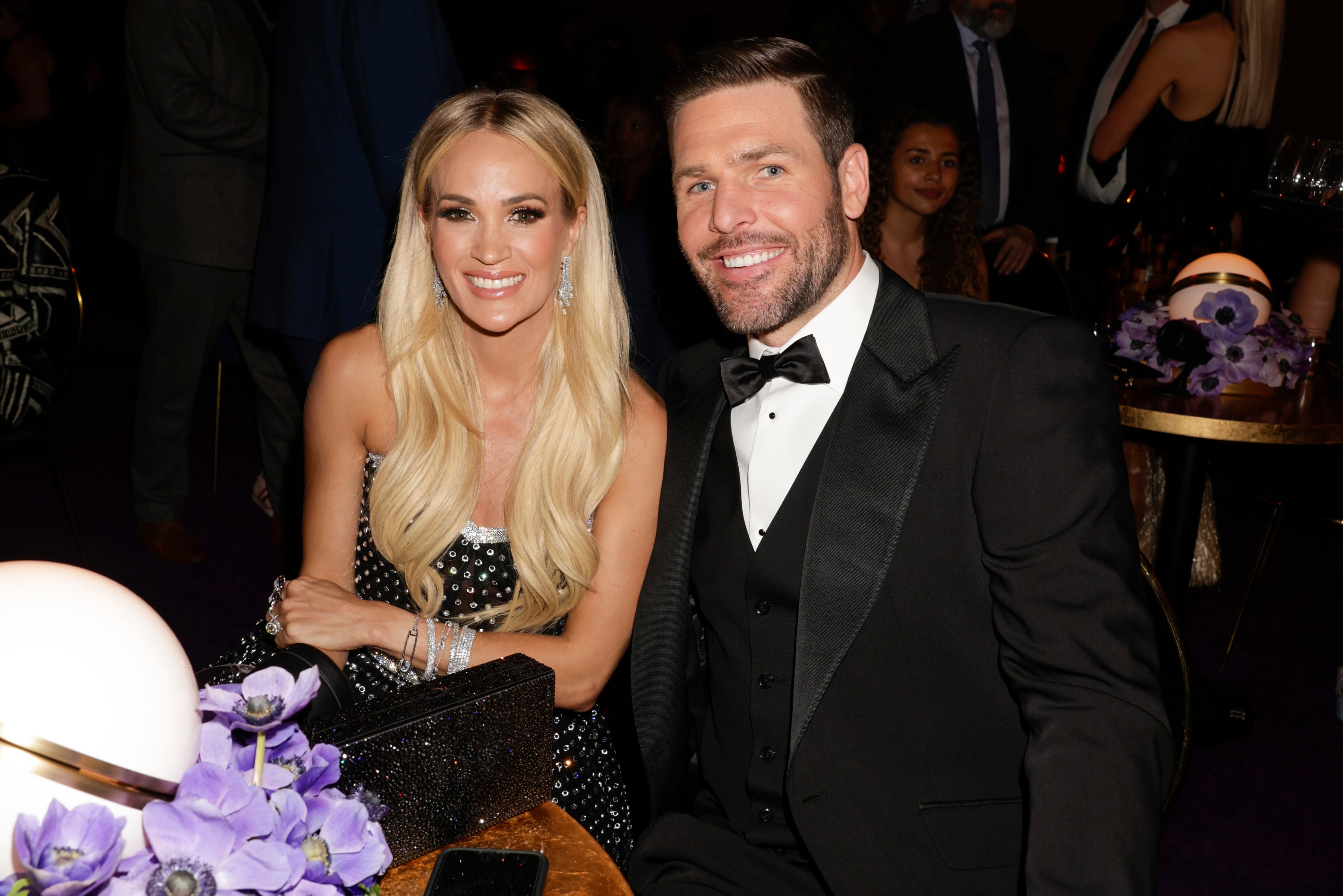 Carrie Underwood and Mike Fisher smile at a camera while sitting together at a table