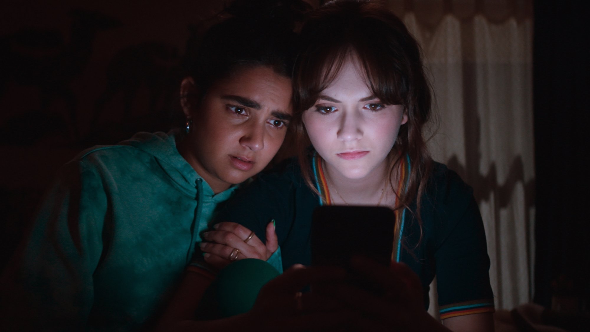 'Cat Person' Geraldine Viswanathan as Taylor and Emilia Jones as Margot looking shocked in a dark room lit by Margot's phone.