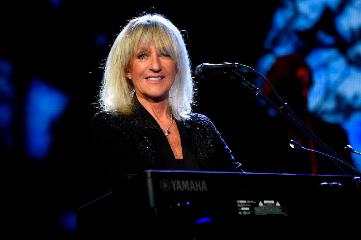 Christine McVie performs on stage, seated at a keyboard with a microphone.