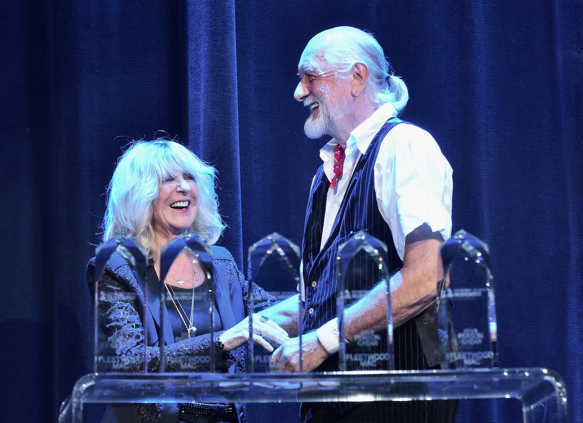Fleetwood Mac stars Christine McVie and Mick Fleetwood laugh on stage together.