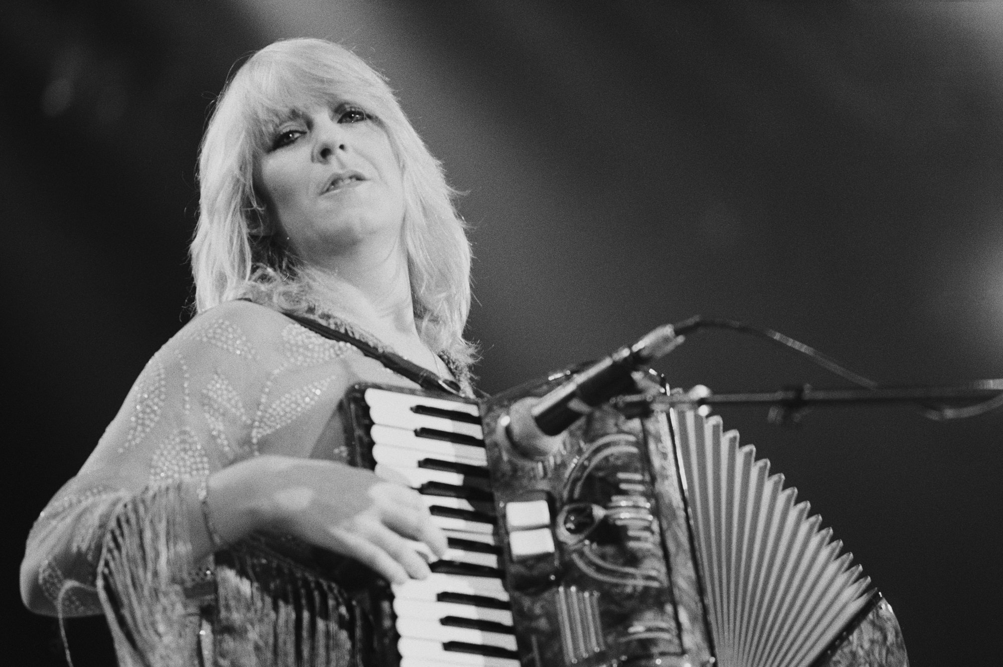 A black-and-white photo of Christine McVie playing the accordion on stage