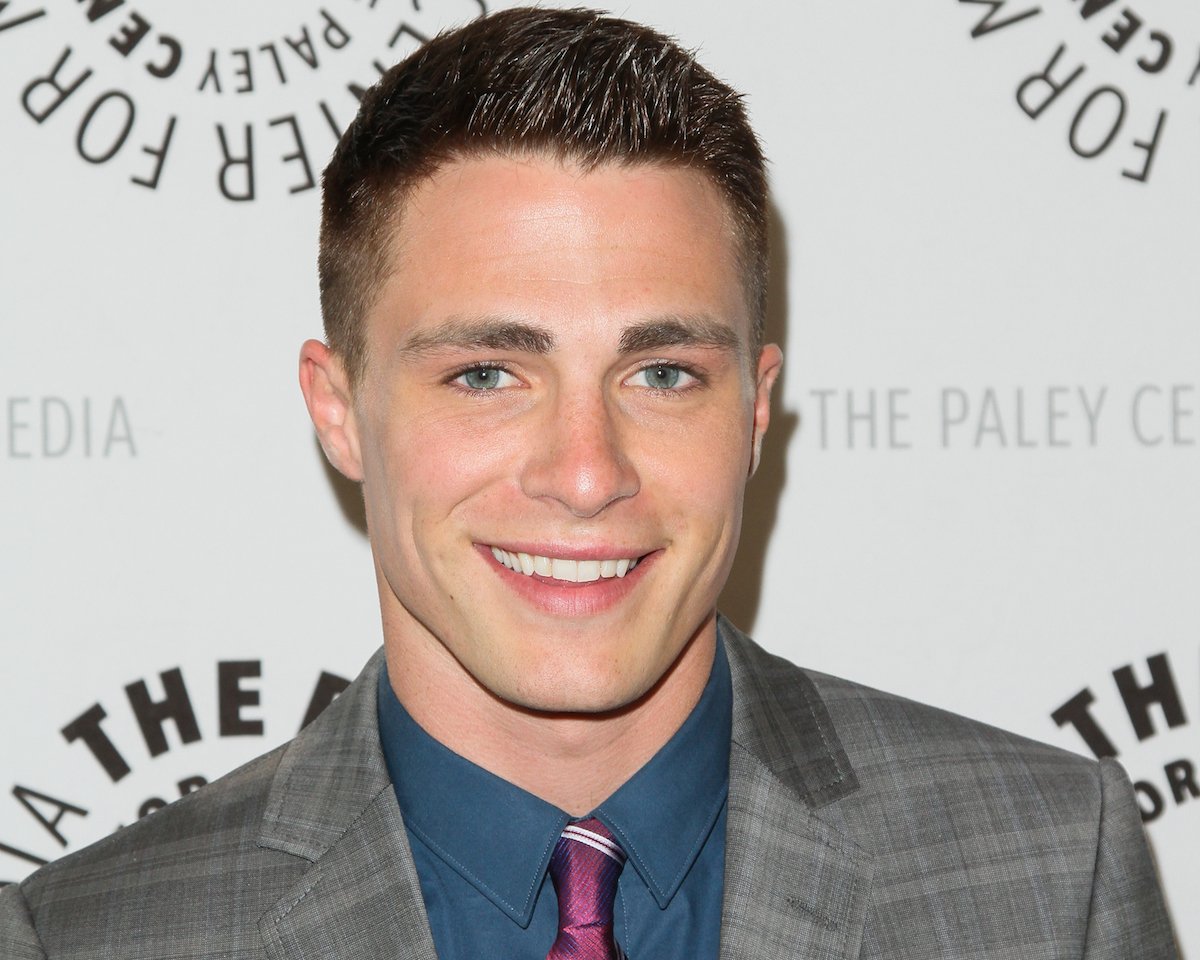 Actor Colton Haynes smiles for the camera, posing in front of a white backdrop.
