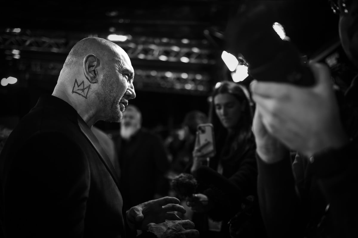 A black and white image of Dave Bautista in profile posing for photos at an event promoting "Glass Onion"