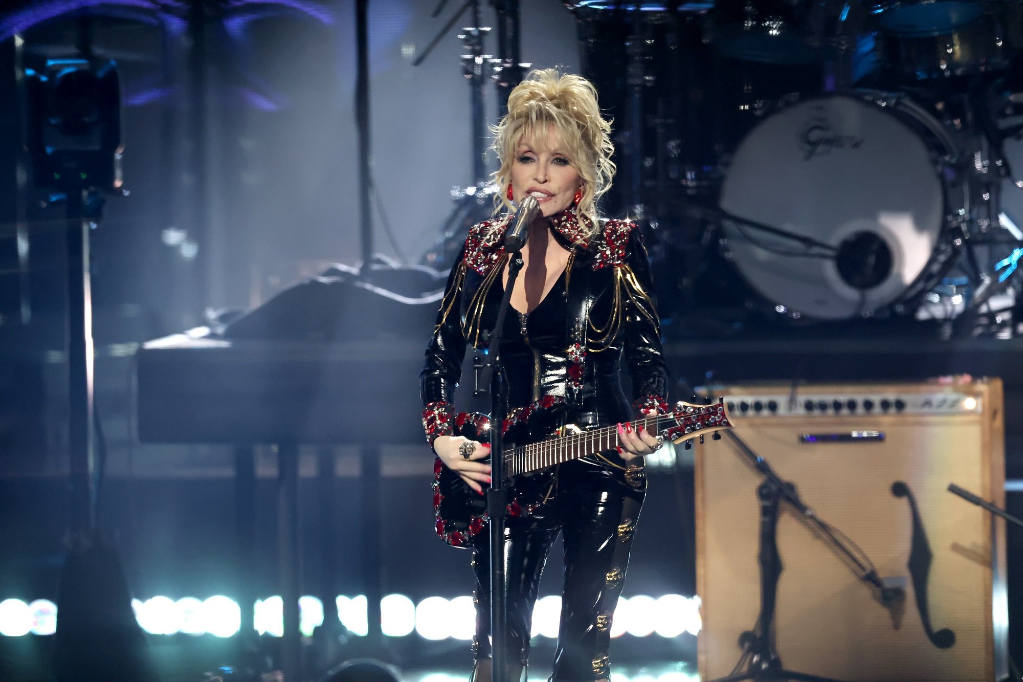 Dolly Parton performs on stage with a guitar while wearing a black leather outfit