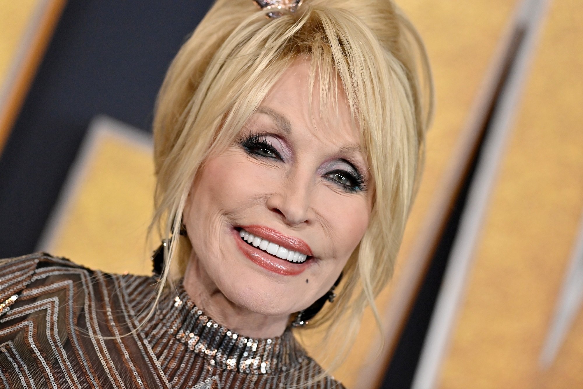 Dolly Parton smiles in front of a gold backdrop