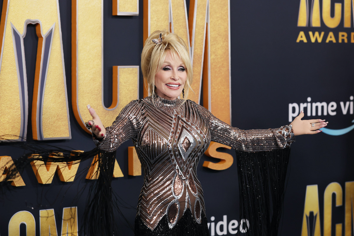 Dolly Parton, known for writing the Whitney Houston hit 'I Will Always Love You,' poses with her arms outstretched. 
