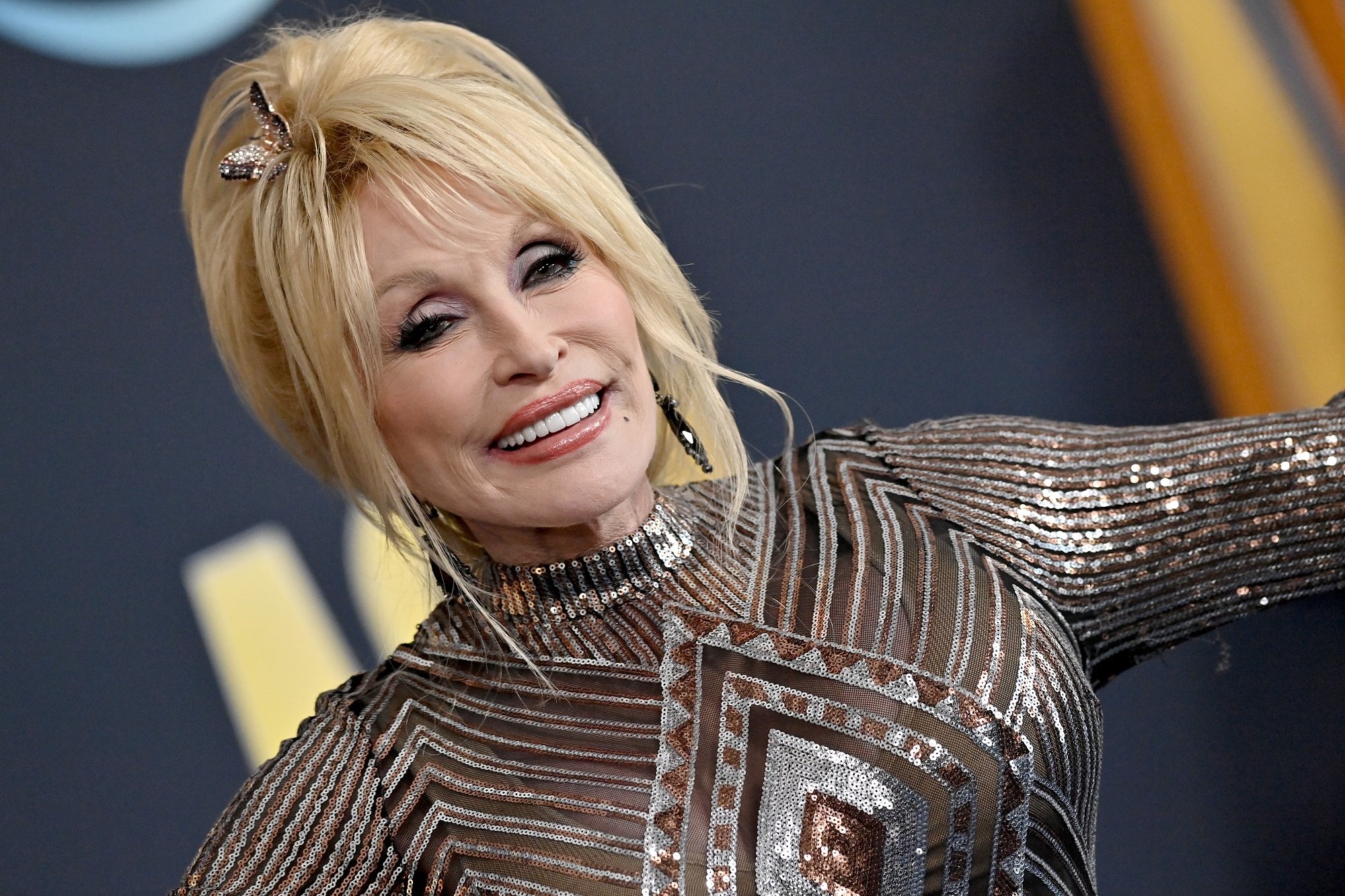 Dolly Parton smiles at the camera wearing a gold and silver dress