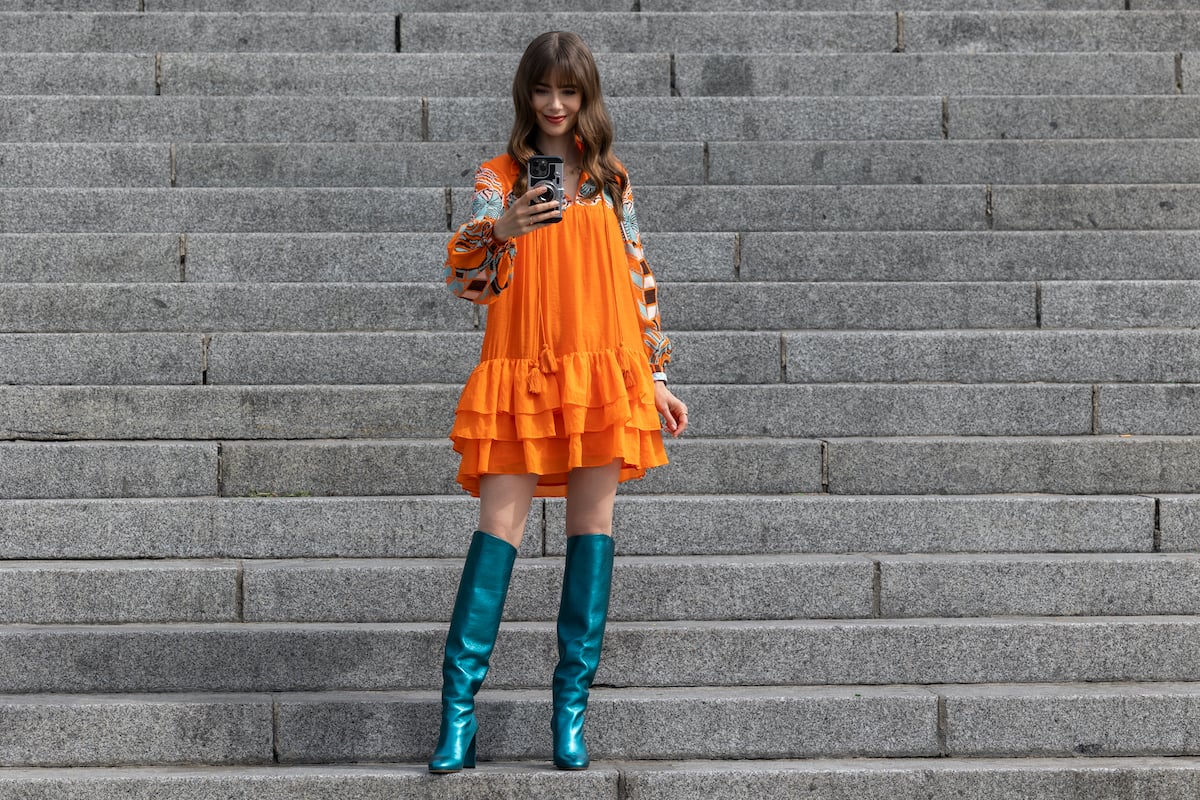 'Emily in Paris' star Lily Collins as Emily Cooper wearing an orange dress with a ruffle trim and metallic teal knee high boots