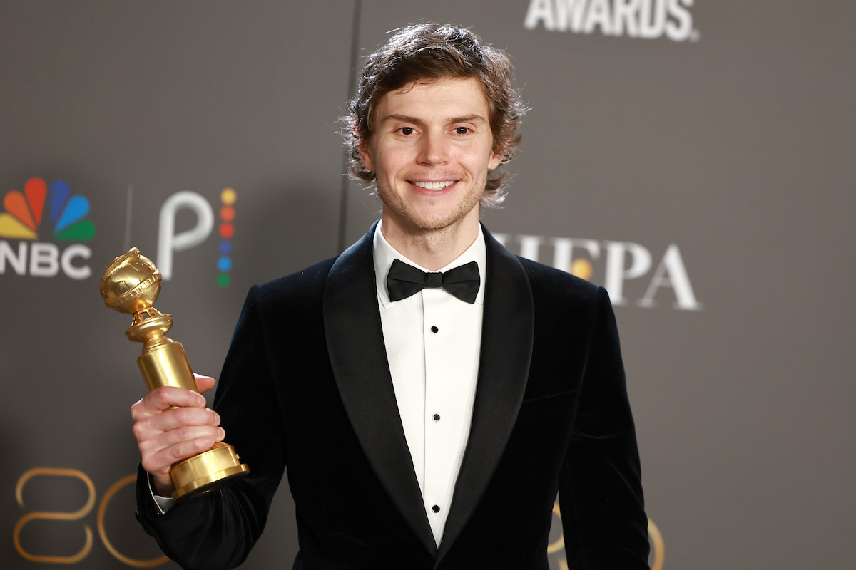 "American Horror Story" star Evan Peters smiles and holds a Golden Globe Award.