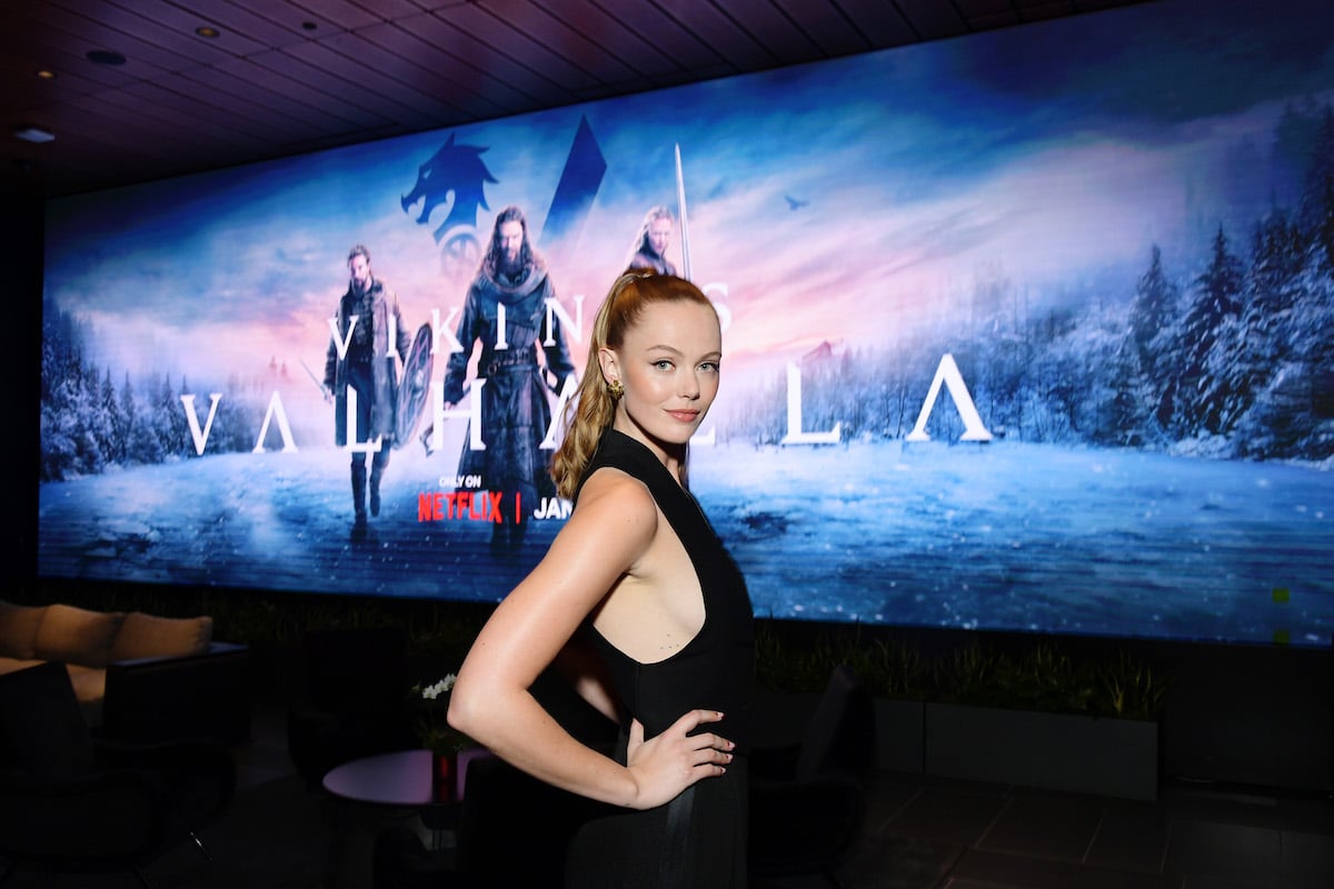 Frida Gustavsson poses in front of an image featuring the key art from Netflix's "Vikings: Valhalla."