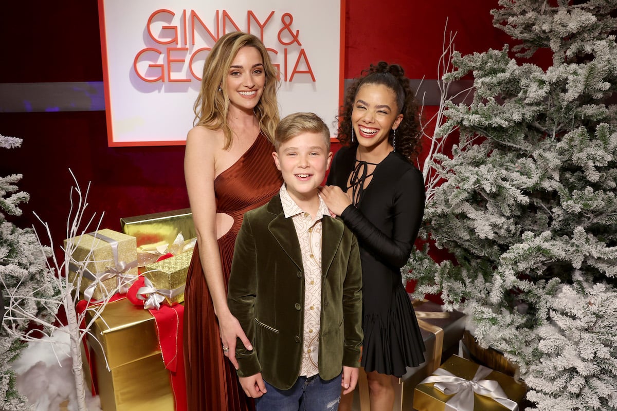 rianne Howey, Diesel La Torraca and Antonia Gentry pose in front of a Christmas themed backdrop in front of the "Ginny and Georgia" logo.