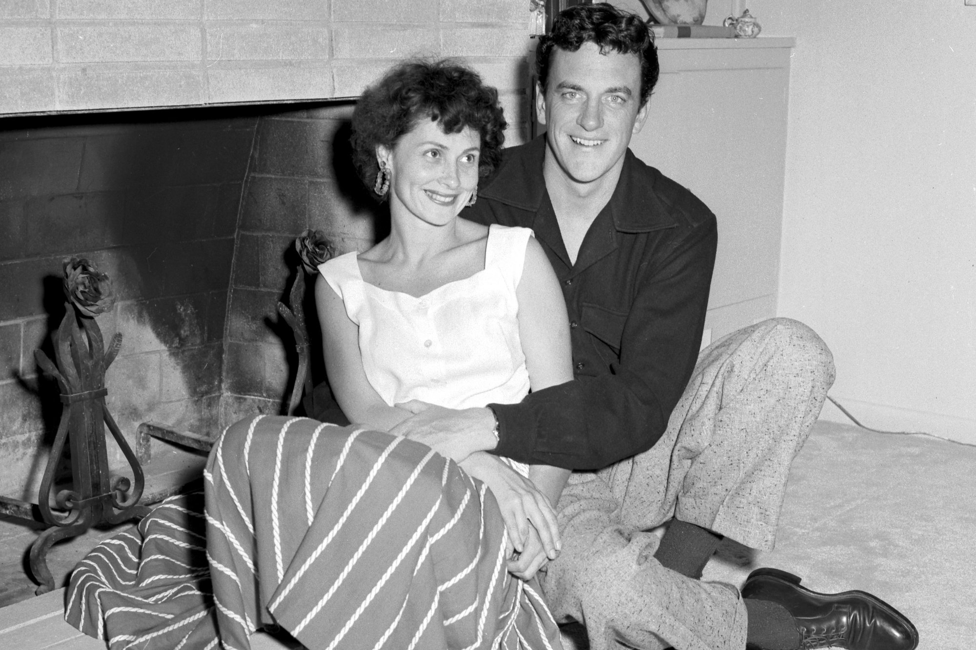 'Gunsmoke' Virginia Arness and James Arness sitting in front of their fireplace. James has his arm wrapped around Virginia.