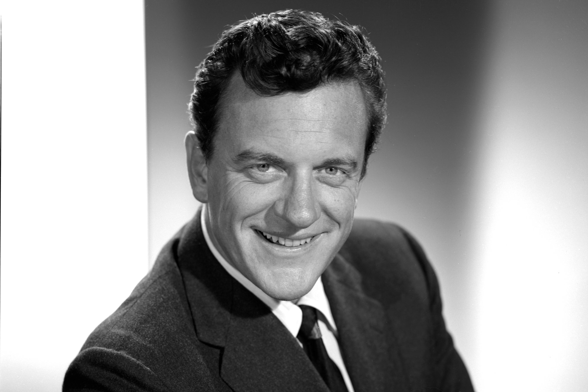 'Gunsmoke' actor James Arness smiling in a black-and-white promo image wearing a suit and tie