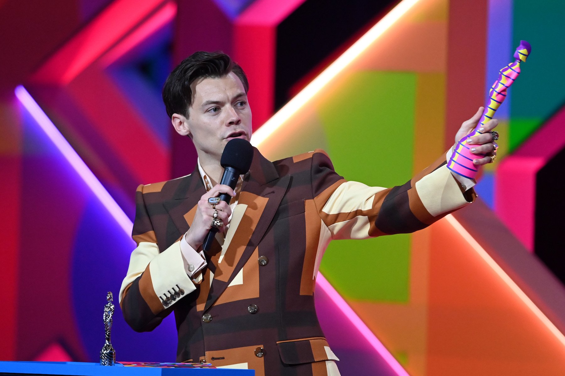 Grammy-winning singer Harry Styles, nominated for Record of the Year in 2023 alongside artists like Doja Cat, on stage wearing a brown striped suit
