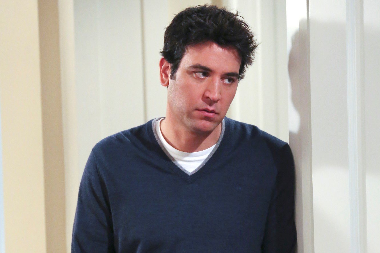 Josh Radnor, in character as Ted Mosby in 'How I Met Your Mother,' wears a dark blue sweater over a white shirt. Radnor recently teased that he would be open to reprising his role as Ted in 'How I Met Your Father' on Hulu.