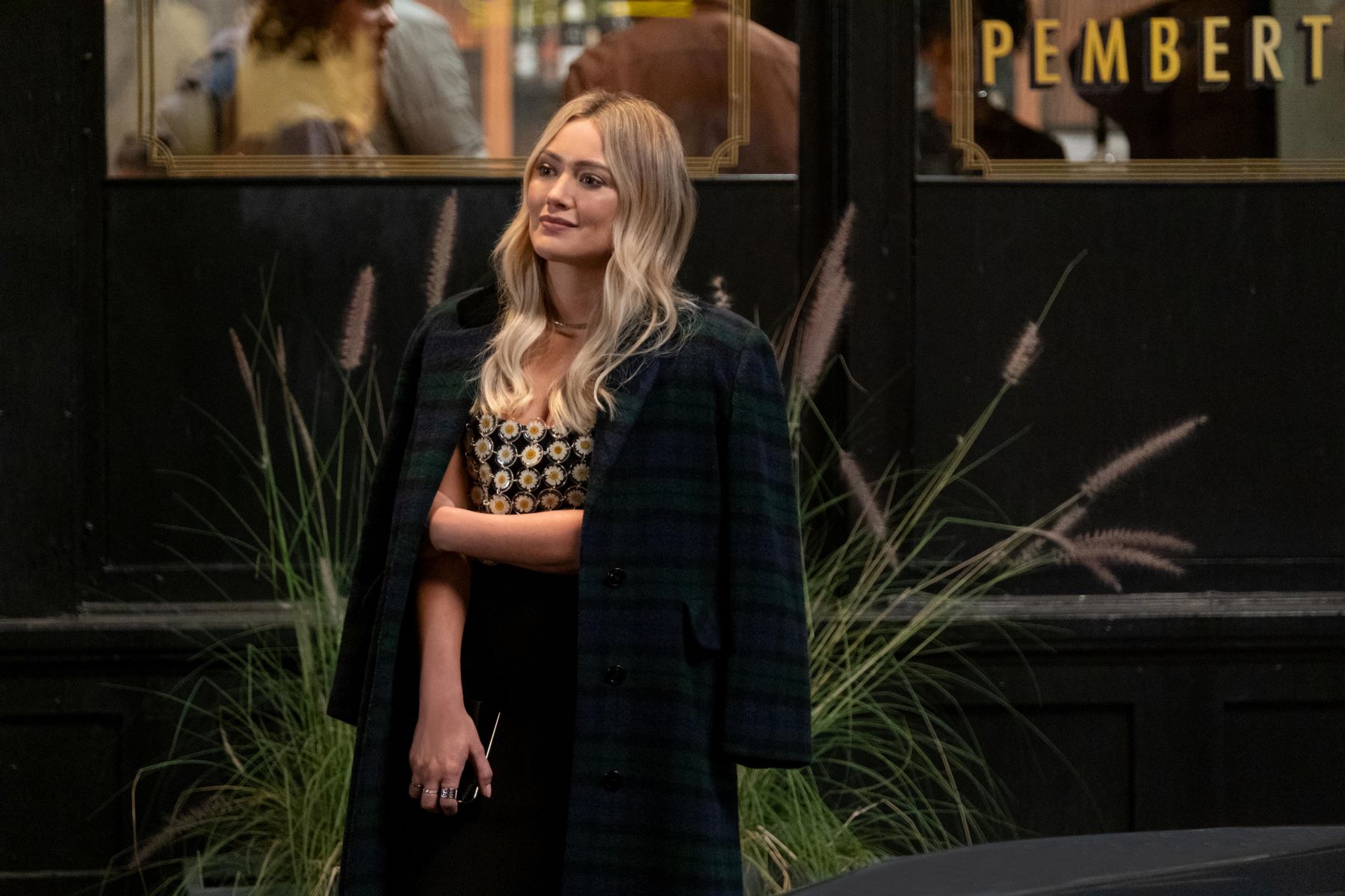 Hilary Duff, in character as Sophie in 'How I Met Your Father' Season 2 Episode 1, wears a dark blue and green plaid coat over a daisy tank top and black skirt.