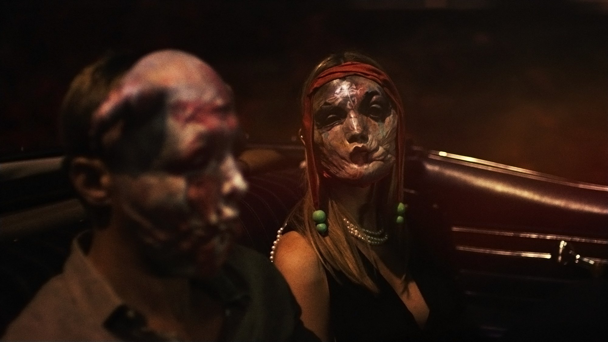 'Infinity Pool' Alexander Skarsgård as James Foster and Mia Goth as Gabi sitting in a car wearing Ekki masks.