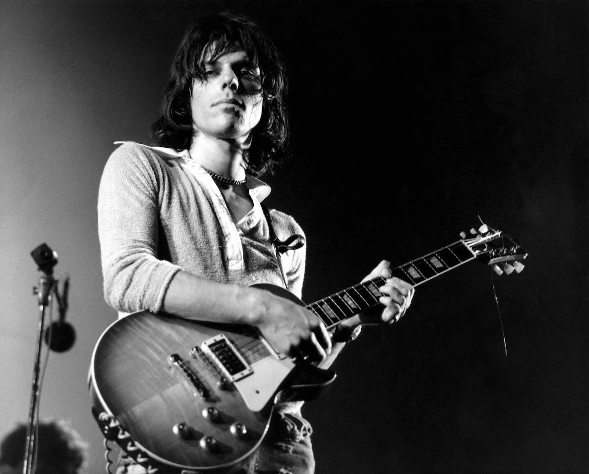 A black and white photo of Jeff Beck holding a guitar and looking at the camera.