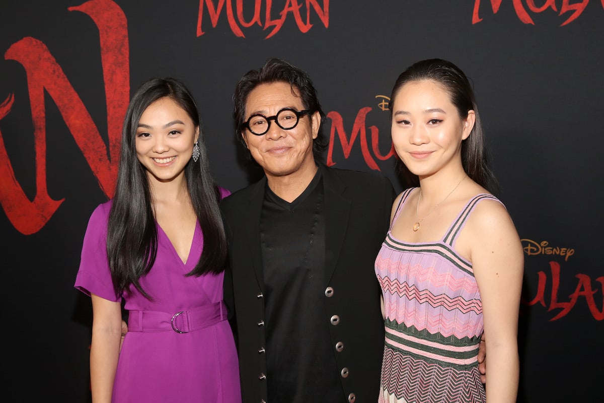 Jet Li and daughters Jane and Jada pose in front of a backdrop featuring the "Mulan" logo
